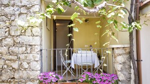Ein Steinhaus mit einem Balkon, auf dem sich ein Tisch und Stühle befinden, umgeben von Blumentöpfen und Blumen.