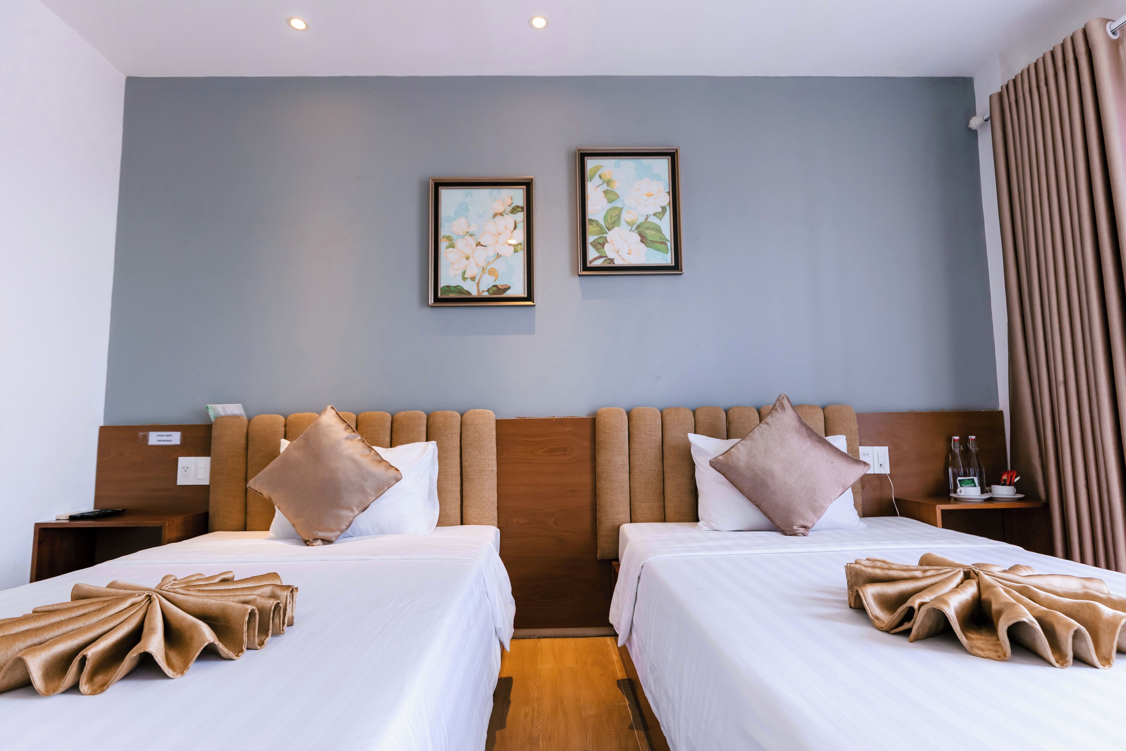 A hotel room with two beds, a wooden headboard, a nightstand, and a small table with a bottle and glasses.