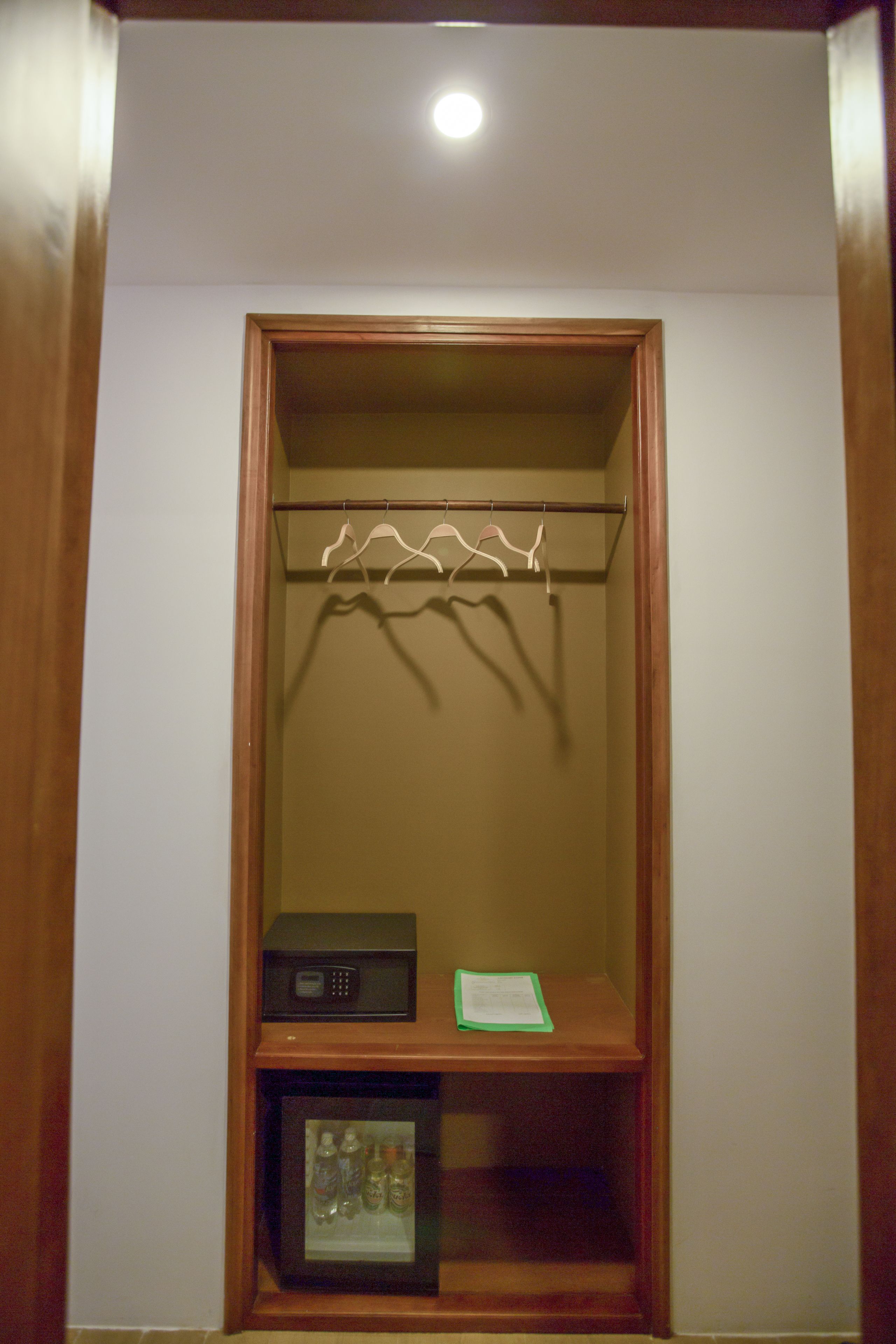 A wooden closet with a hanging rod, a small shelf with a radio, and a lower shelf with bottles.