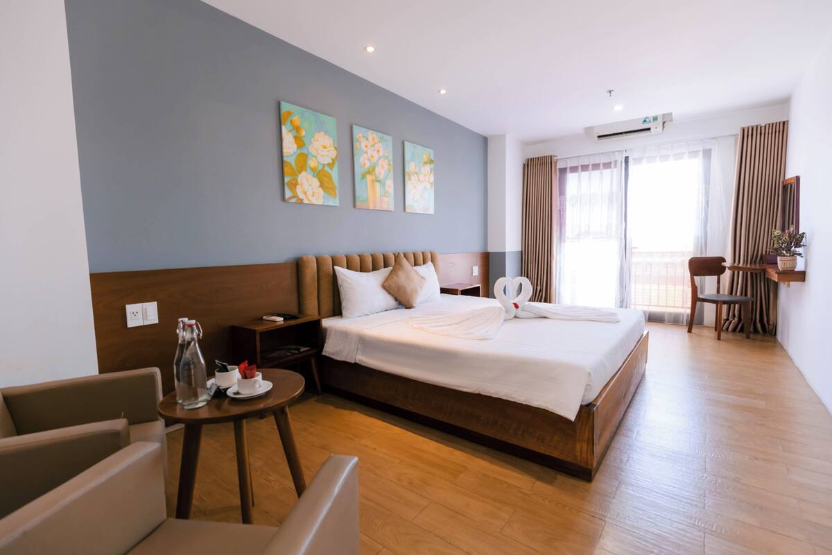 Ein Hotelzimmer mit einem großen Bett, einem Nachttisch, einem Sessel, einem kleinen Tisch und einem Fenster mit Vorhängen.
