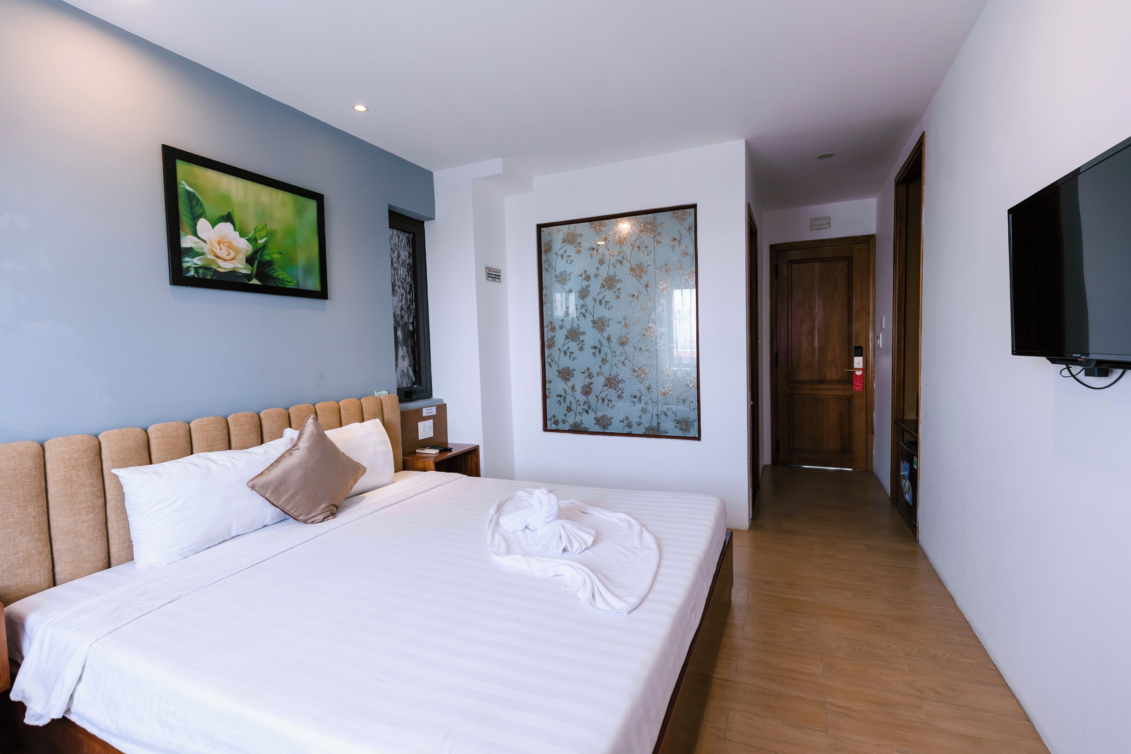 A hotel room with a bed, a painting, a television, and a wooden floor.