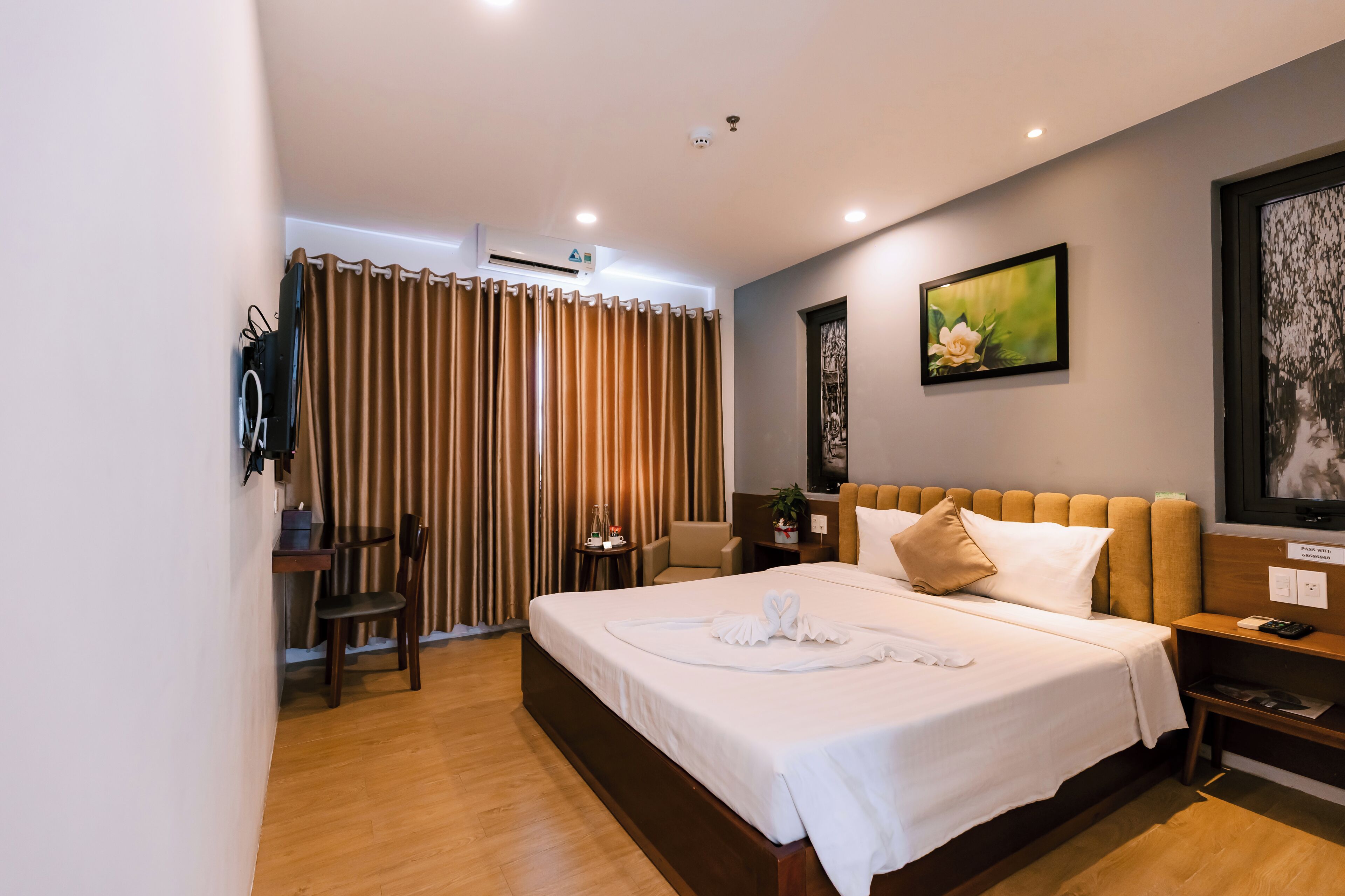 A hotel room with a large bed, a desk, a chair, a small table with a plant, and a painting on the wall.