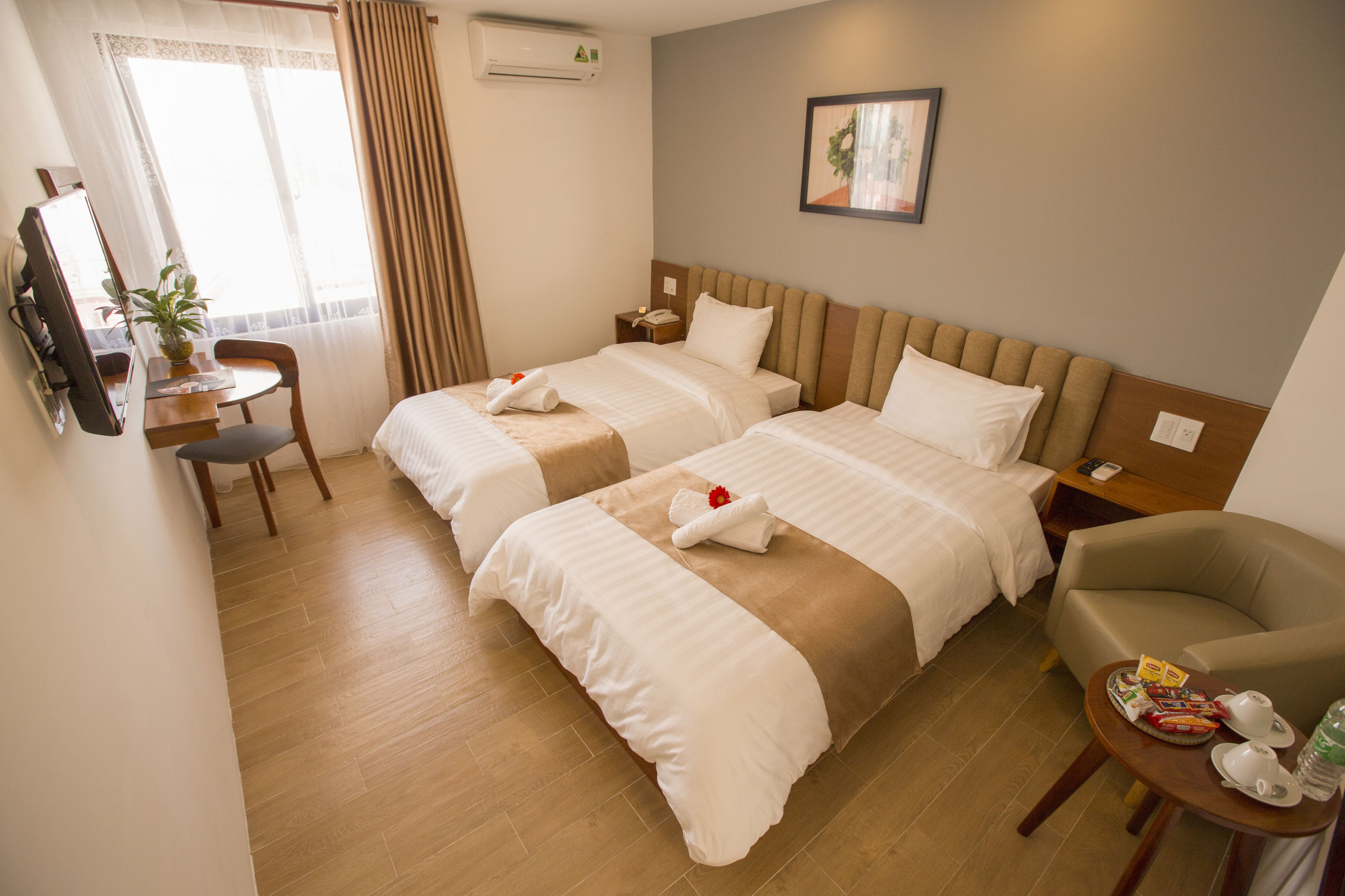 Een hotelkamer met twee bedden, een bureau, een stoel, een klein tafeltje met theepot en kopjes, en een lijst aan de muur.