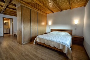 A bedroom with a wooden bed, a nightstand, a wardrobe, and a bathroom visible through an open door.