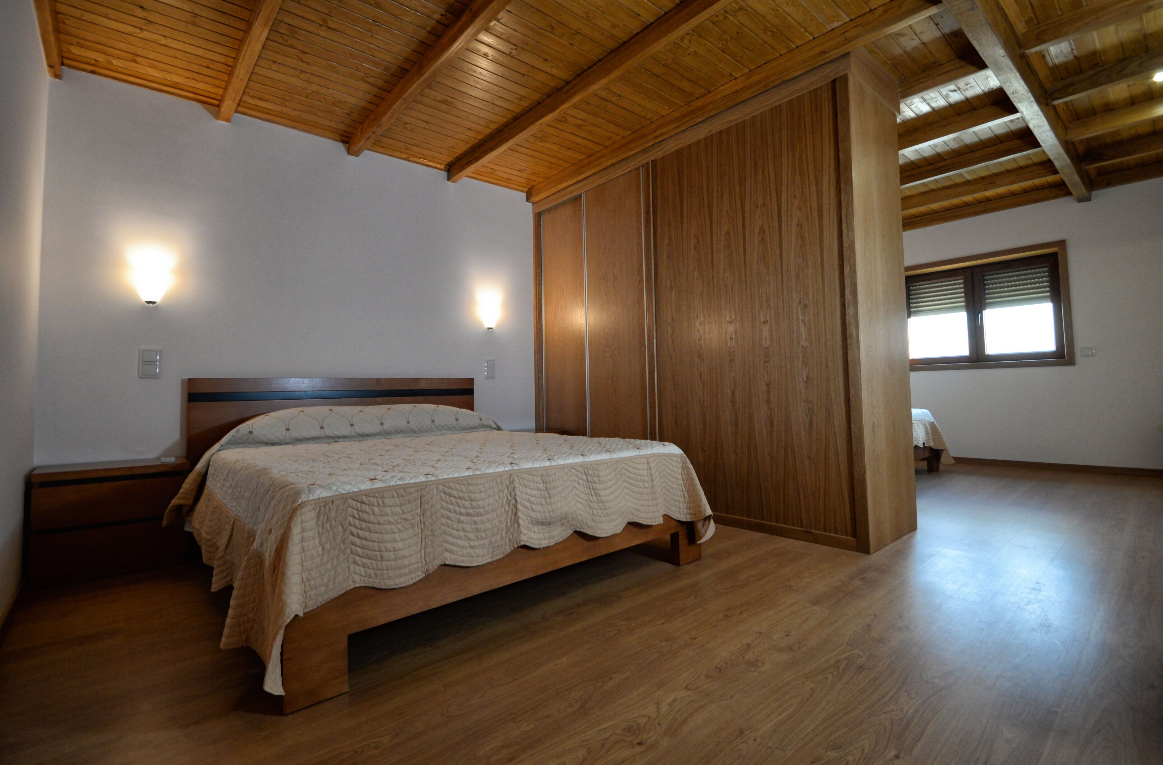 Quarto com cama de madeira, paredes de madeira, teto inclinado e janela com persianas.