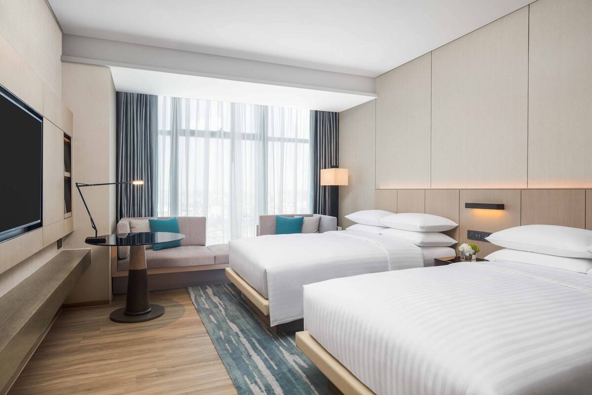 Hotelkamer met twee bedden, een zithoek, een flatscreen-tv en een groot raam met gordijnen.