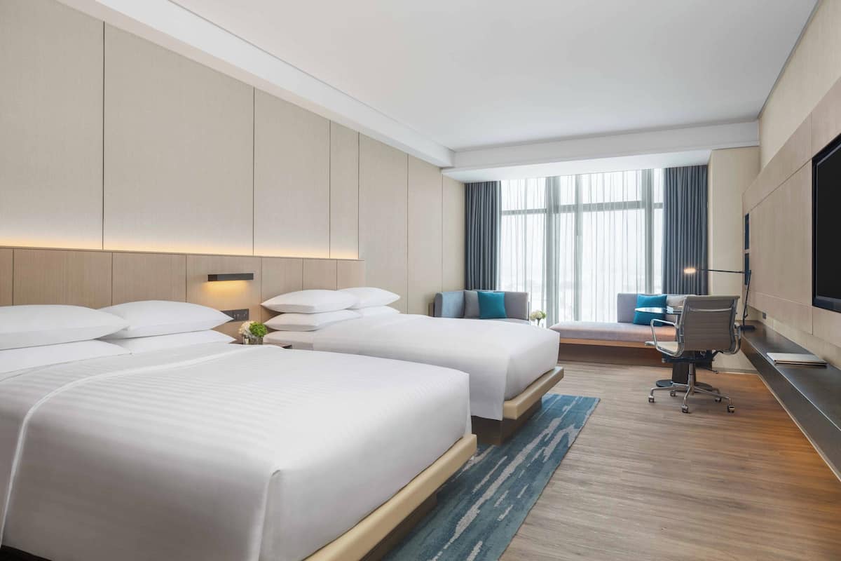Een hotelkamer met twee bedden, een bureau, een stoel, een televisie en een groot raam.