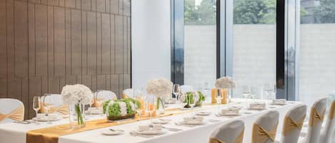 Una larga mesa de comedor dispuesta para un evento formal, con manteles blancos, fajas doradas y centros de mesa con flores blancas.
