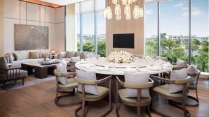 Un espace repas moderne avec une table ronde, plusieurs chaises, un lustre et une grande fenêtre donnant sur la ville.