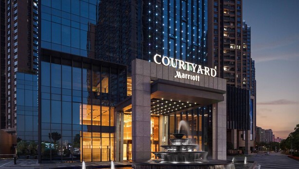 Un hôtel Courtyard Marriott avec une fontaine devant, entouré d’immeubles de grande hauteur.