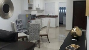 A modern living room with a black sofa, a dining area with patterned chairs, and a kitchen in the background. - Condo P (Mazatlán)