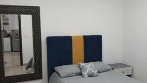 A bedroom with a bed, a nightstand, a mirror, and a wall-mounted shelf. - Condo P (Mazatlán)