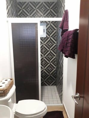 A bathroom with a shower, toilet, and patterned wall tiles.