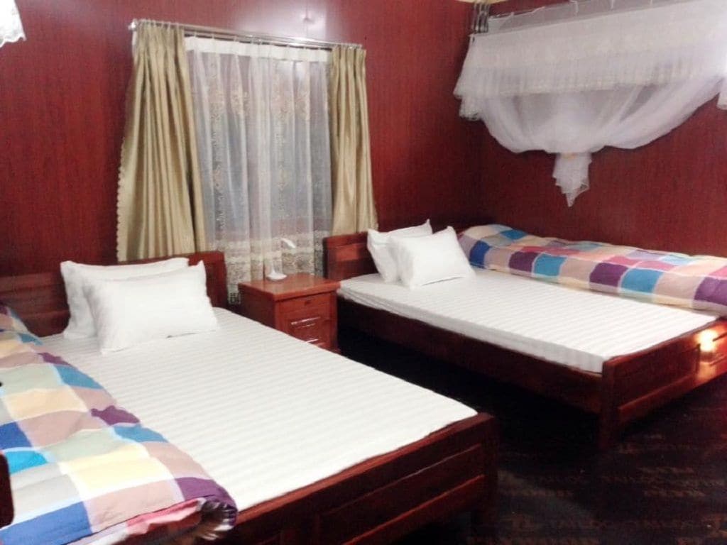 Habitación de hotel con dos camas individuales, una mesita de noche de madera y una ventana con cortinas.
