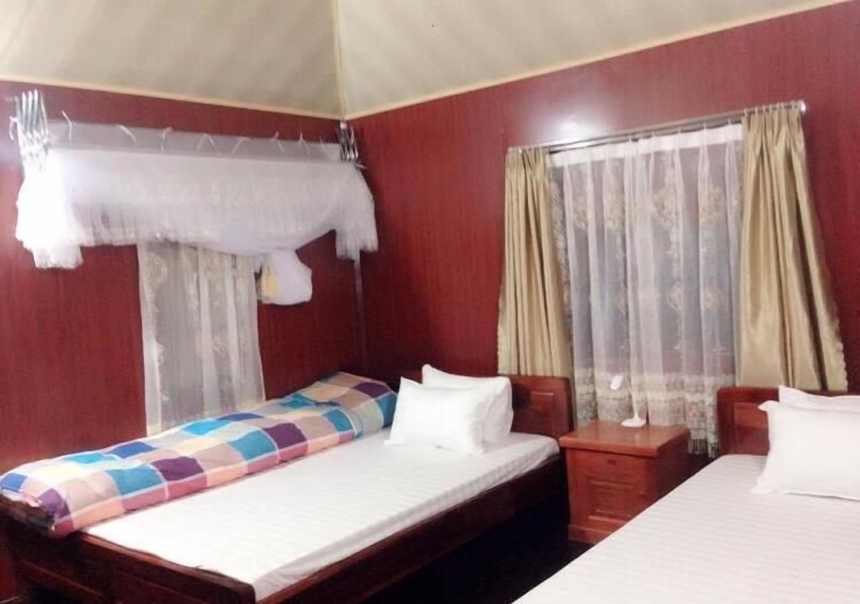 Une chambre d’hôtel avec deux lits, une tête de lit en bois, une table de chevet et une fenêtre avec des rideaux.