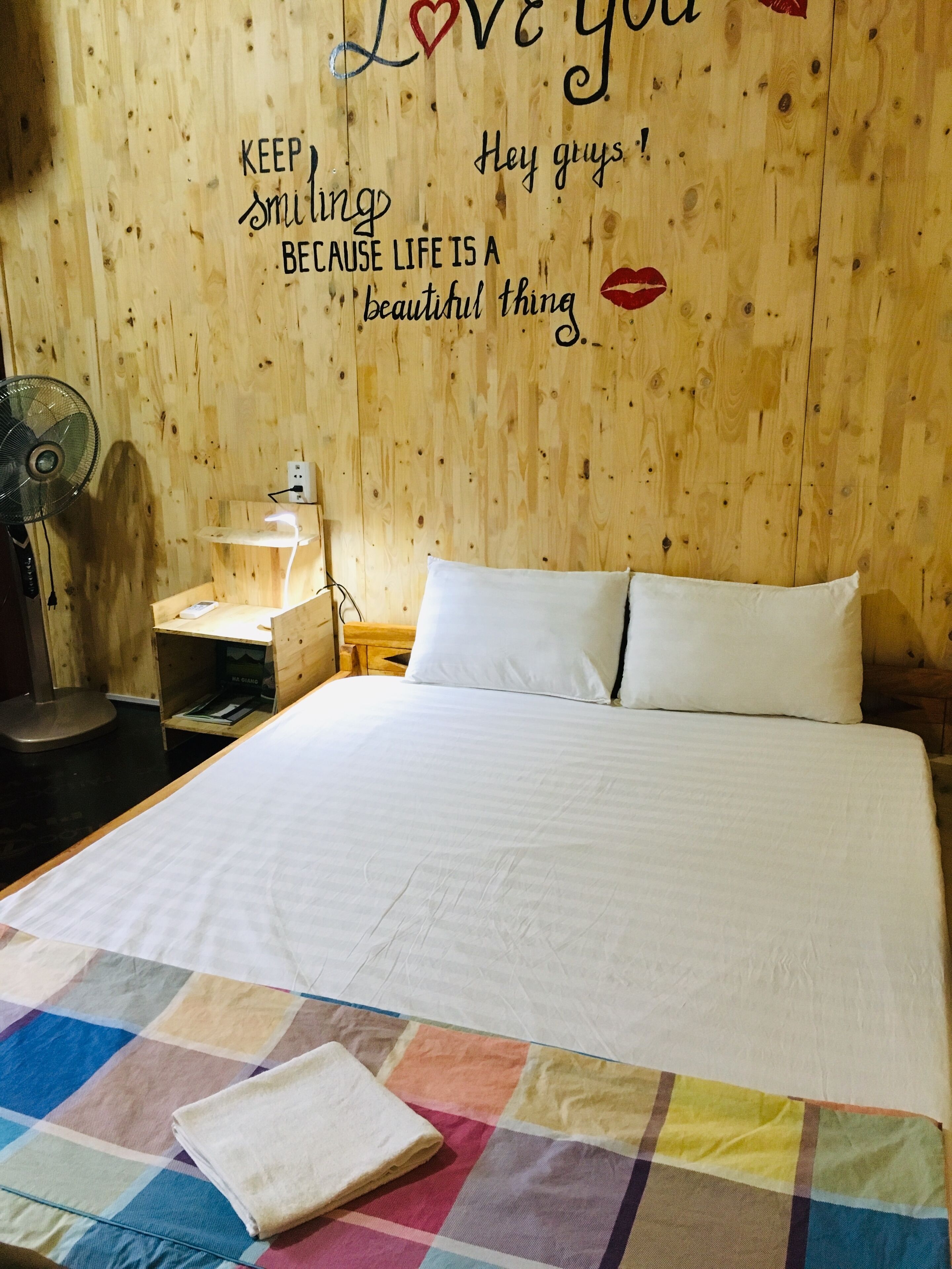 Ein gemütliches Schlafzimmer mit einer Holzwand, einem Bett mit weißer Bettwäsche, einer farbenfrohen Bettdecke und einem Nachttisch mit einer Lampe.