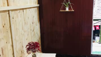 A wooden room with a small table and a vase of red flowers. There are three hanging plant shelves on the wall.