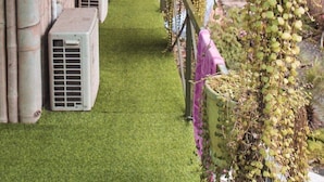 A covered outdoor area with air conditioning units, a grassy path, and hanging plants. - Green Hill Hostel & Homestay (Ha Giang 2)