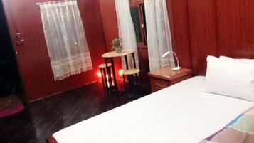 A bedroom with a bed, a small table, a chair, and a desk with a lamp.