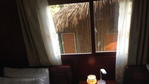 A room with two beds, a table with a lamp, and a window with a thatched roof view. - Green Hill Hostel & Homestay (Ha Giang 2)