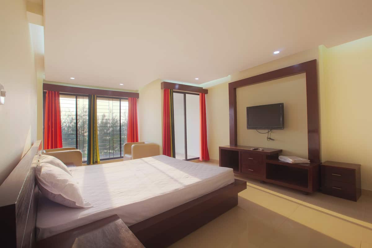 A hotel room with a large bed, a TV mounted on the wall, a desk with drawers, and a chair.
