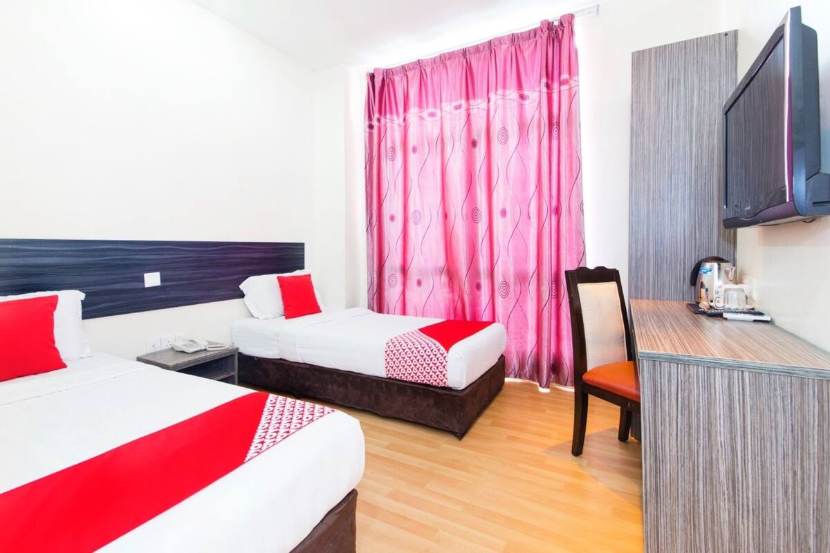 A hotel room with two beds, a desk, a chair, a television, and a window with curtains.
