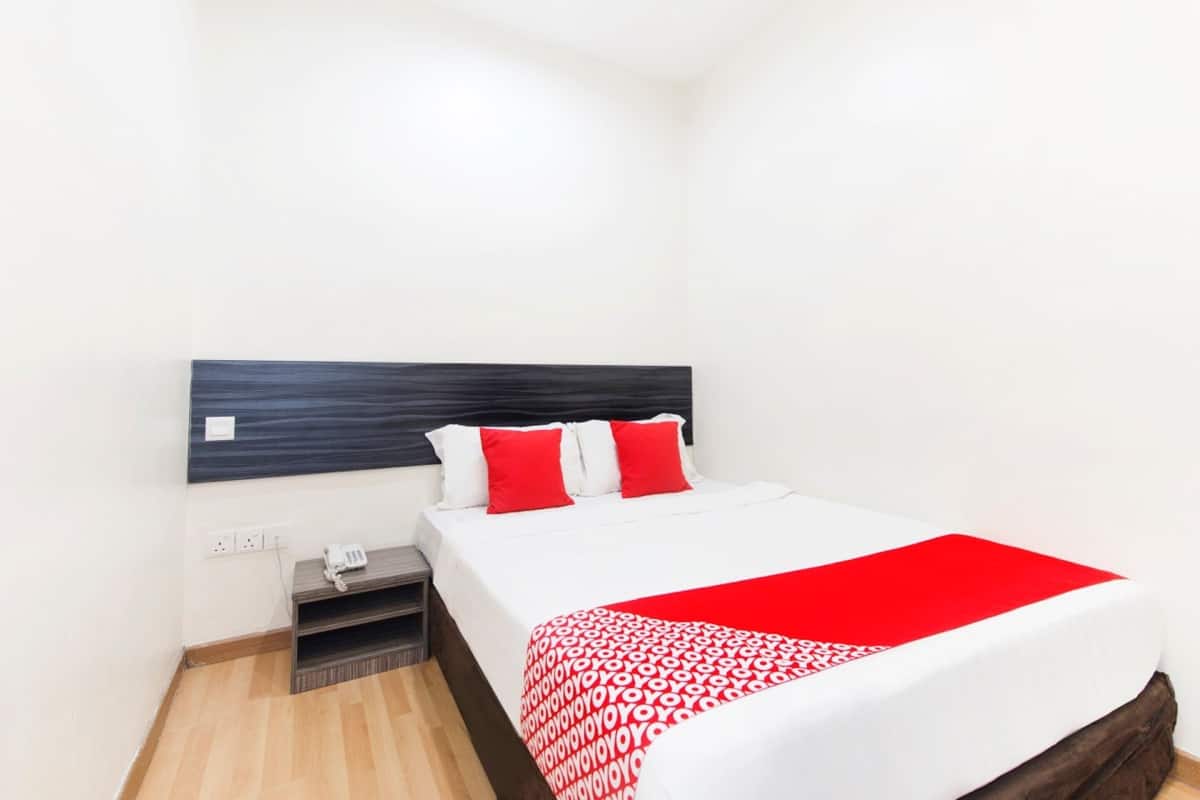 A hotel room with a bed, a bedside table, a phone, and a power outlet.