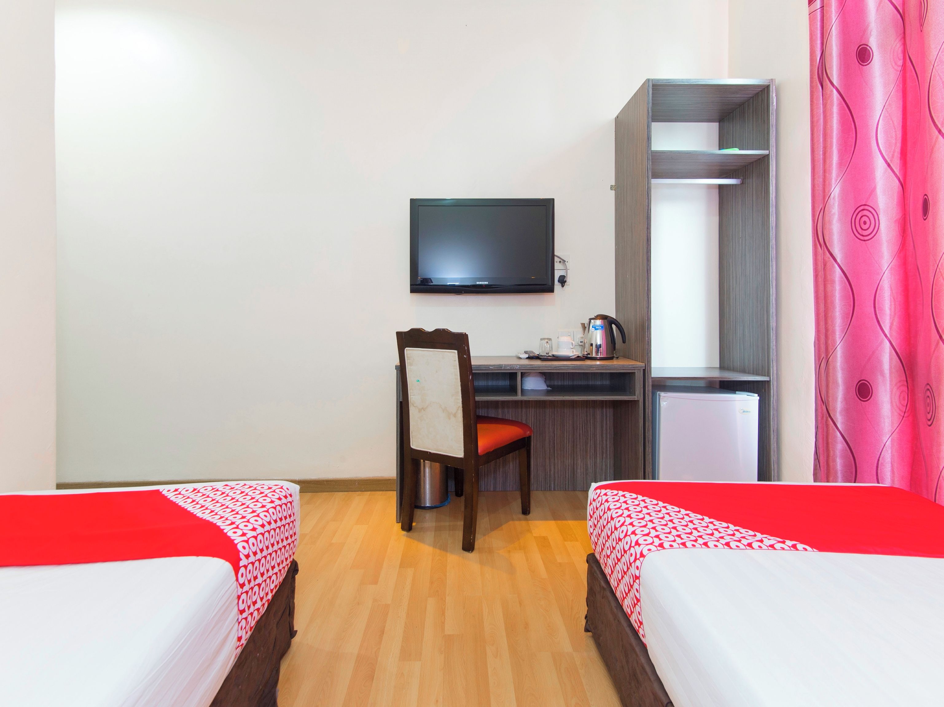 A hotel room with two beds, a desk, a chair, a television, and a wardrobe.