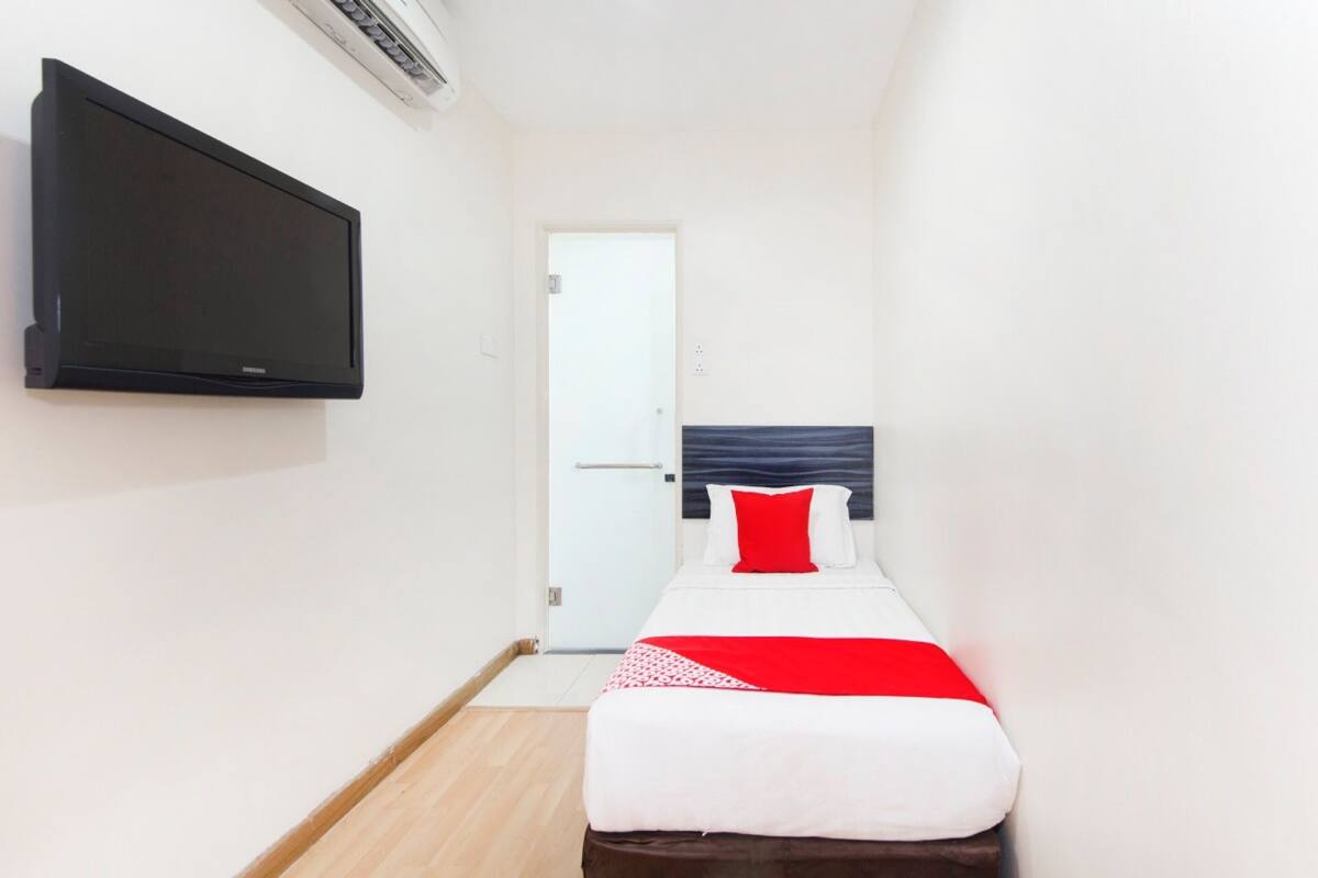 A hotel room with a bed, a flat-screen TV mounted on the wall, and a door leading to another room.