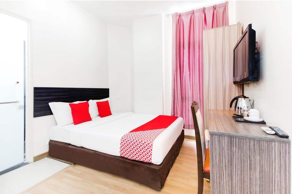 A hotel room with a bed, a desk, a television, and a window with curtains.