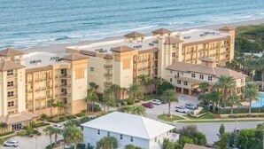 Un hotel junto a la costa con varias edificaciones, vistas a la playa y un aparcamiento con coches.
