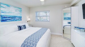 Un dormitorio con cama, ventilador de techo, ventana con persianas, espejo y televisor instalado en la pared.