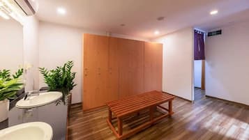 A bathroom with a sink, mirror, potted plants, a wooden bench, and a wardrobe.