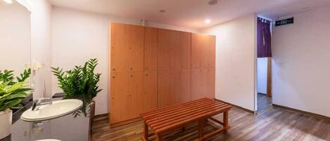 A bathroom with a sink, mirror, potted plants, a wooden bench, and a wardrobe.