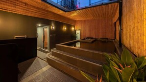 A spa area with a hot tub, wooden walls, and a view of an industrial structure. - Azumaya Hotel Linh Lang (Hanoi)