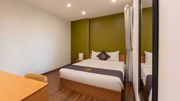 A hotel room with a bed, a desk, and a mirror.