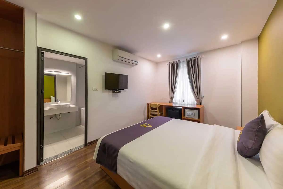 A hotel room with a bed, a desk, a TV, a mirror, and a wardrobe.