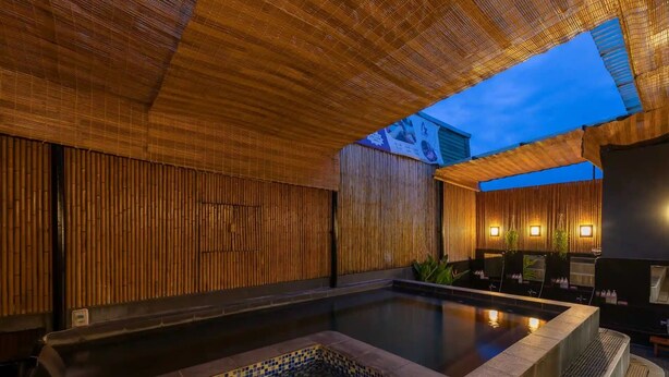 A serene indoor pool area with bamboo walls, a seating area with chairs, and a view of the sky. - Azumaya Hotel Linh Lang (Hanoi)