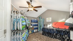 Habitación con ventilador de techo, estanterías con maletas y una tabla de surf.