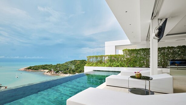 En modern infinitypool med en fantastisk utsikt över havet och ett frodigt, grönskande landskap.
