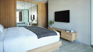 Ein modernes Schlafzimmer mit einem großen Bett, einem Nachttisch, einem Spiegel und einem an der Wand befestigten Flachbildfernseher.