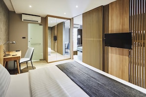 Una habitación de hotel moderna con una cama grande, un escritorio con una silla, un televisor montado en la pared y una puerta corredera que da a un baño.