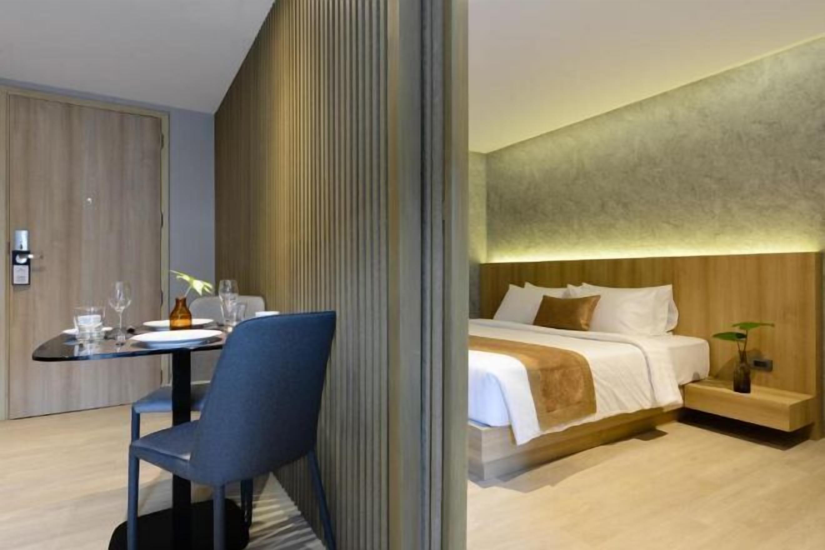 Una habitación de hotel moderna con cama, mesita de noche y zona de comedor con mesa y sillas.