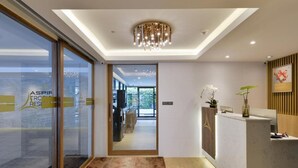 Un espace d’accueil agrémenté d’un lustre moderne, d’un comptoir de réception et d’une porte vitrée donnant sur un couloir.