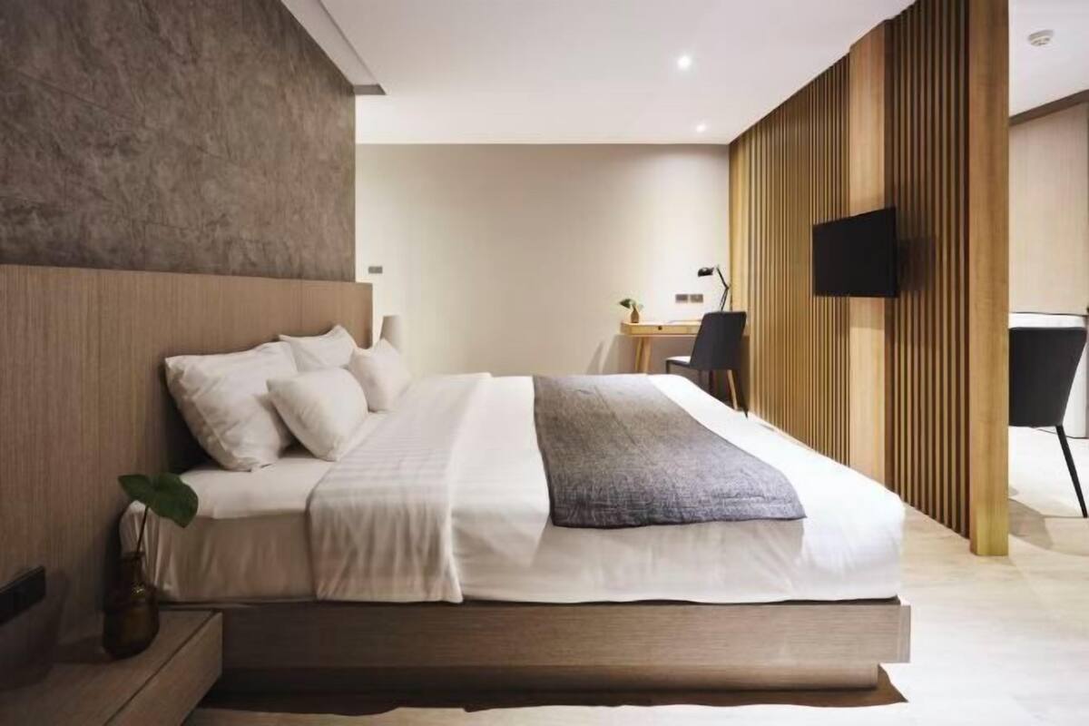 Ein modernes Schlafzimmer mit einem großen Bett, einem Schreibtisch und einem an der Wand befestigten Fernseher.
