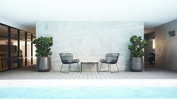 Un espace de détente intérieur moderne, avec deux fauteuils et une table, entouré de grands pots de plantes, le tout adossé à un mur à texture.