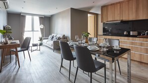 Un espace de repas moderne avec une table dressée pour quatre personnes, un canapé et une cuisine en arrière-plan.