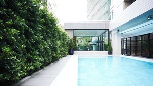 Une piscine intérieure moderne avec une terrasse en bois et une haie verdoyante.