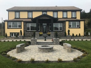 A two-story house with a symmetrical facade, a central entrance with a black door, and a landscaped front yard with a circular stone feature. - Castle Landing (Placentia)