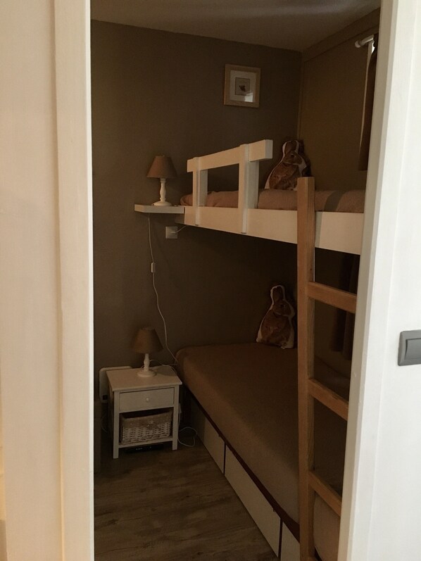 A small, dimly lit room with bunk beds, a nightstand, and a lamp.